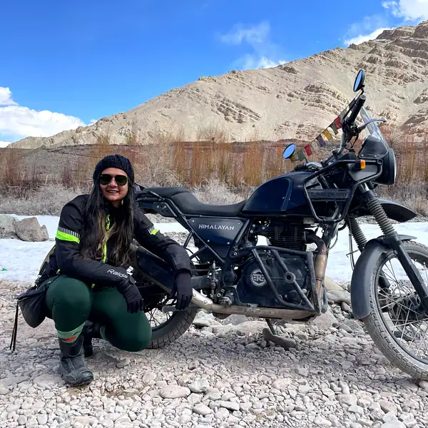 Woman with Himalayan motorcycle in desert landscape.